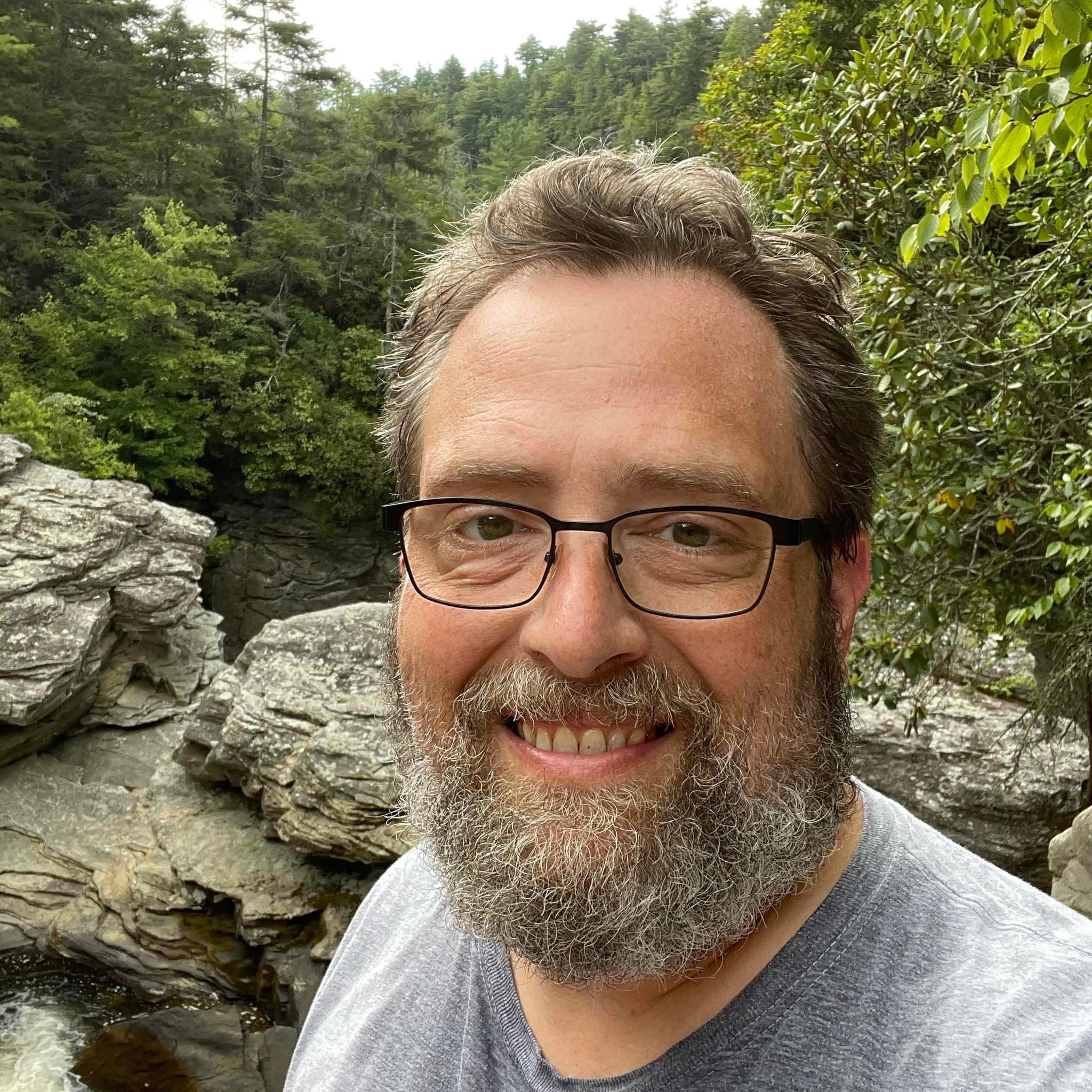 Picture of instructional designer Max Mays, in front of rocks overlooking a forest.
